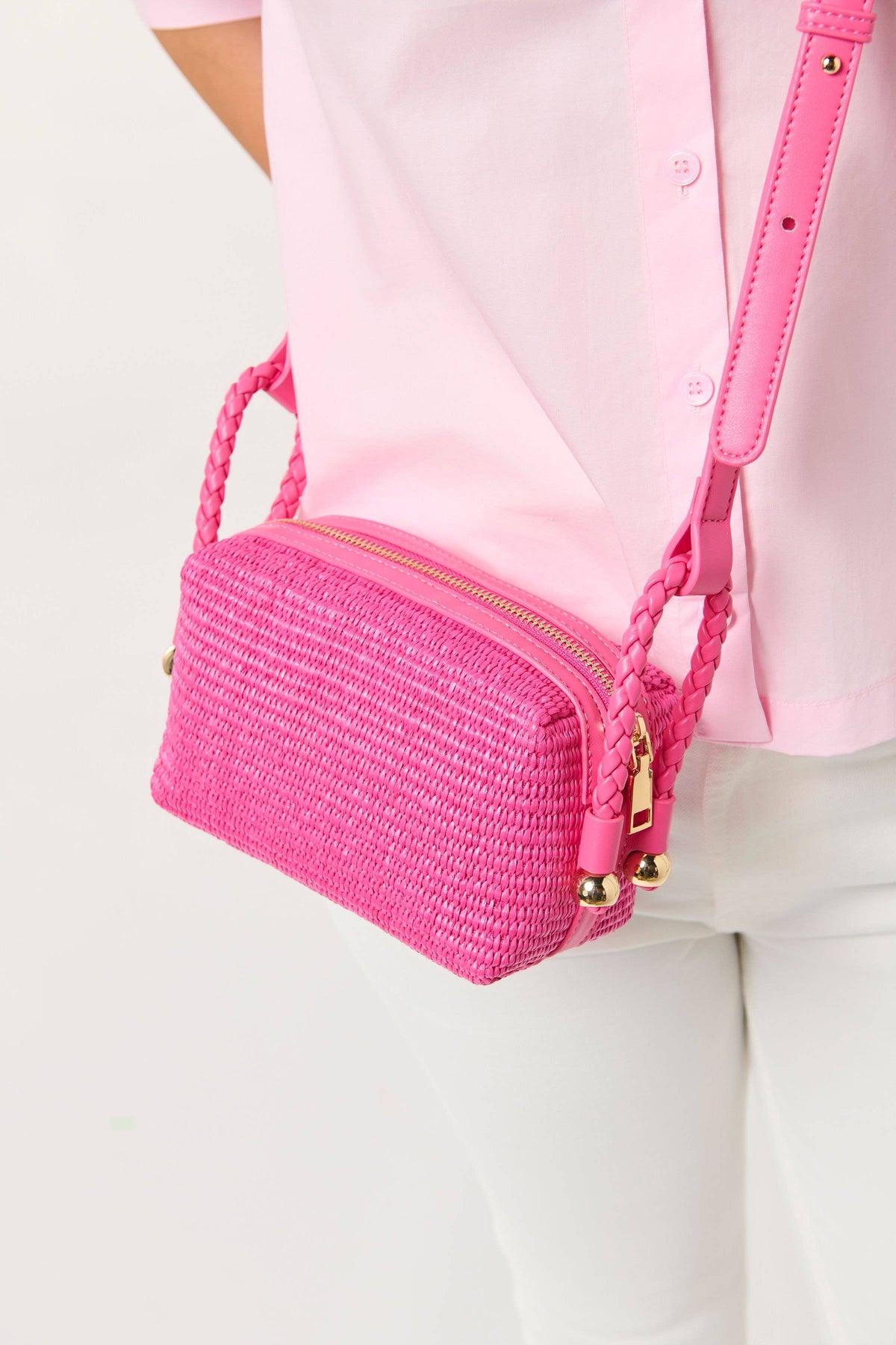 Pink woven handbag with gold accents held by a person wearing a pink shirt and white pants.

